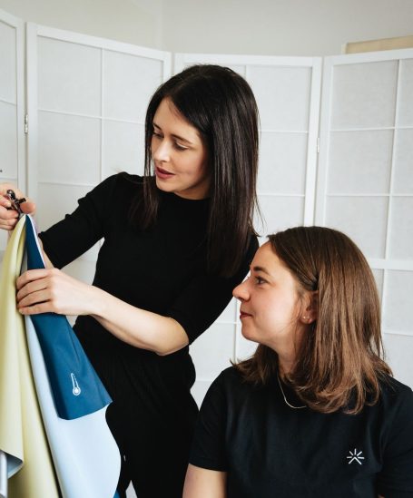 Zwei Frauen betrachten Stoffe, eine zeigt auf einen blauen Stoff.